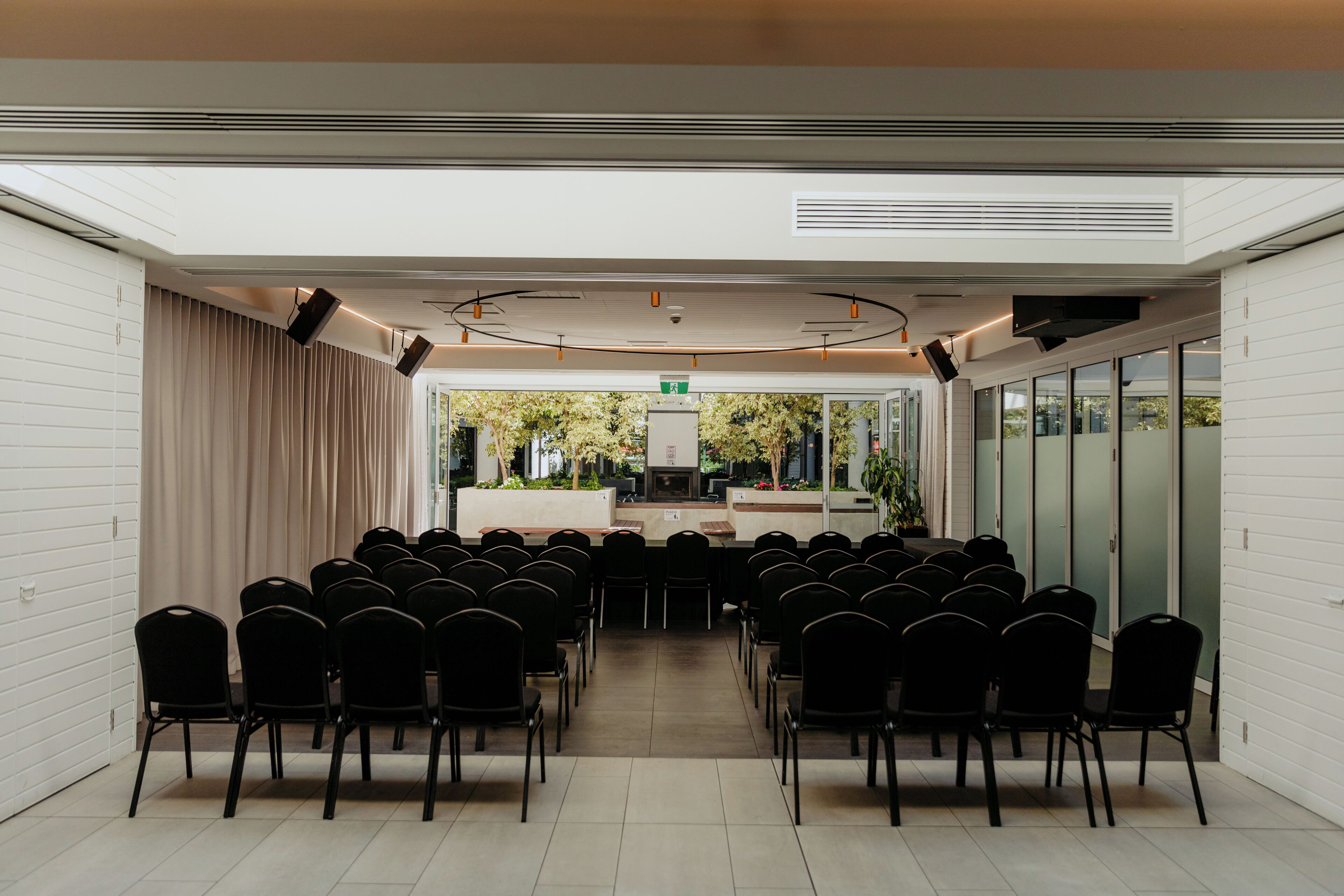 A conference room with rows of chairs, a stage, and a view of greenery outside.