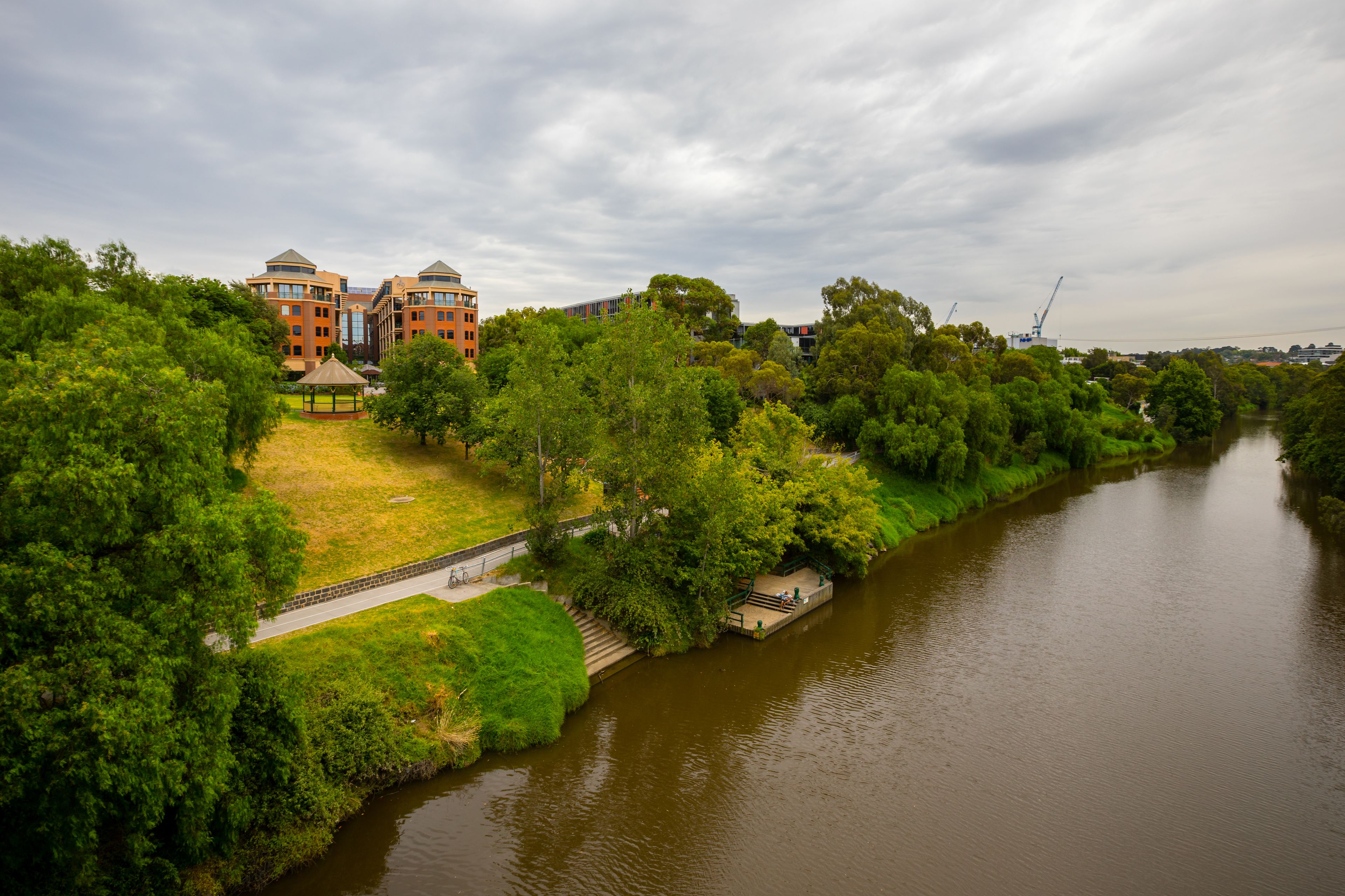 A riverside view with a gazebo, a bridge, and a building with a dome and multiple windows.