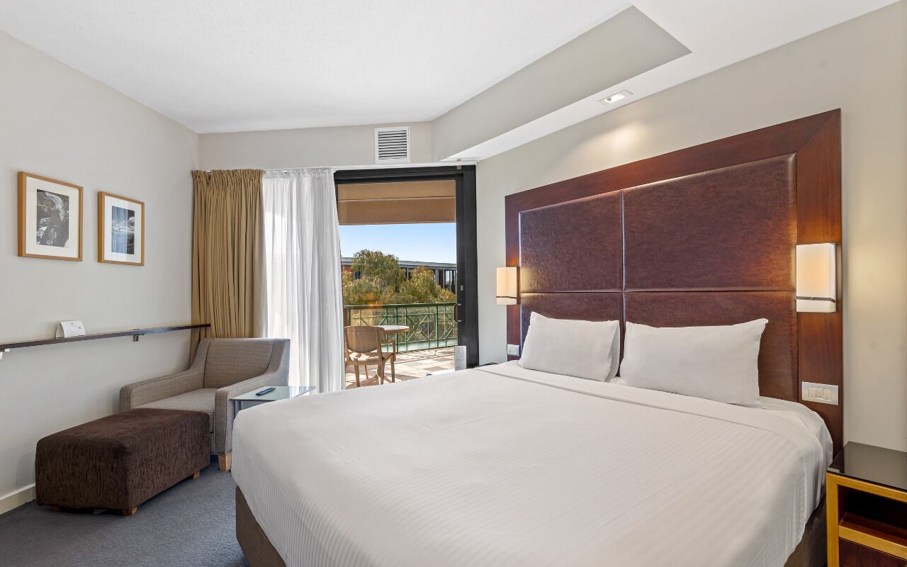Een hotelkamer met een groot bed, een bureau, een stoel, een kleine tafel en een balkon met uitzicht.