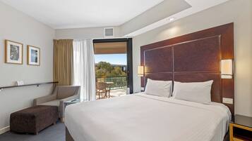 A hotel room with a large bed, a desk, a chair, and a balcony with a view.