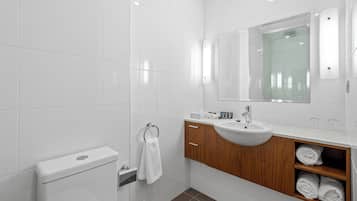 A modern bathroom with white tiles, a wooden vanity, a sink, a toilet, and a towel rack.