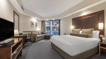 Habitación de hotel con una cama grande, un escritorio con televisor de pantalla plana, un sofá y vistas al balcón.