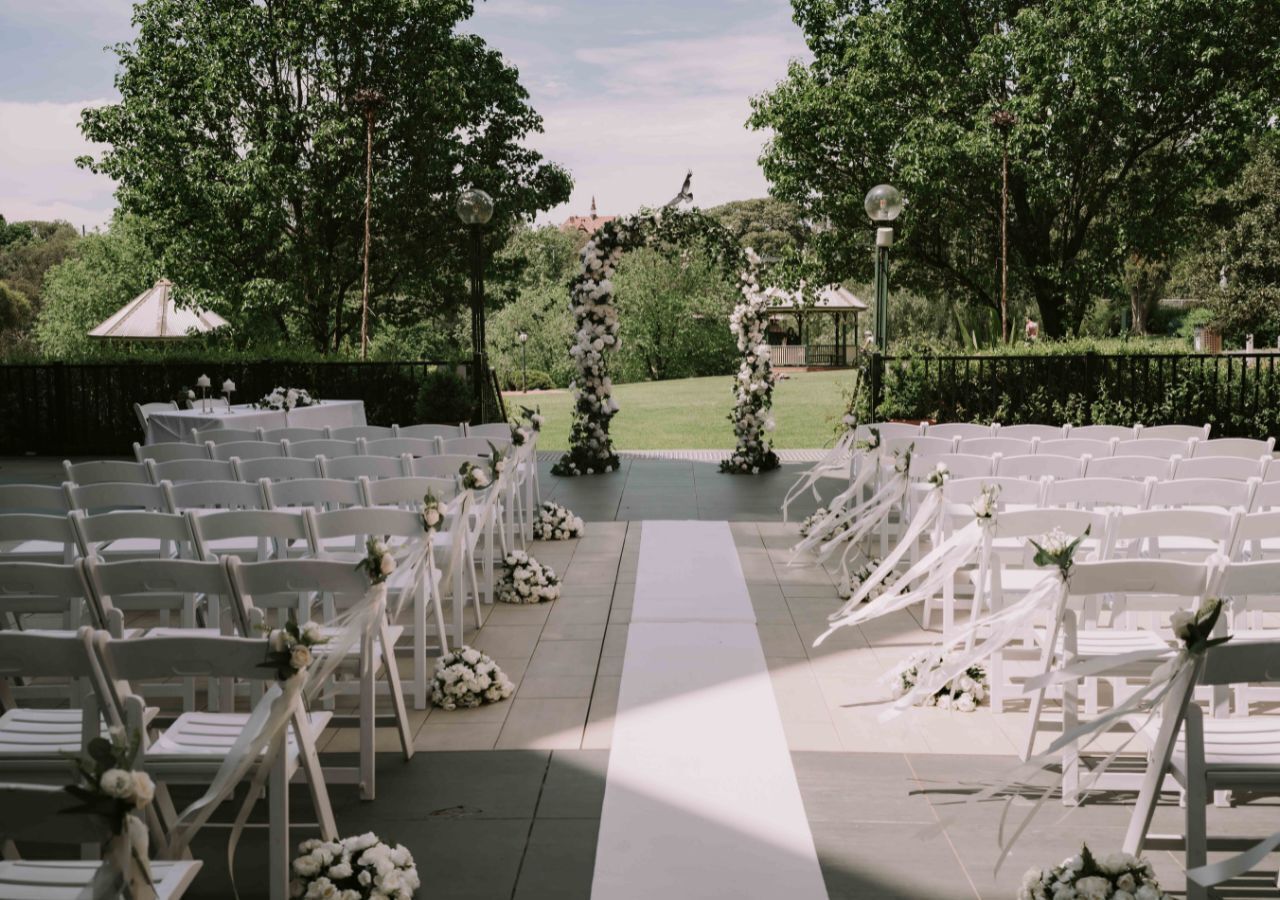 An outdoor wedding aisle with white chairs and floral decorations.