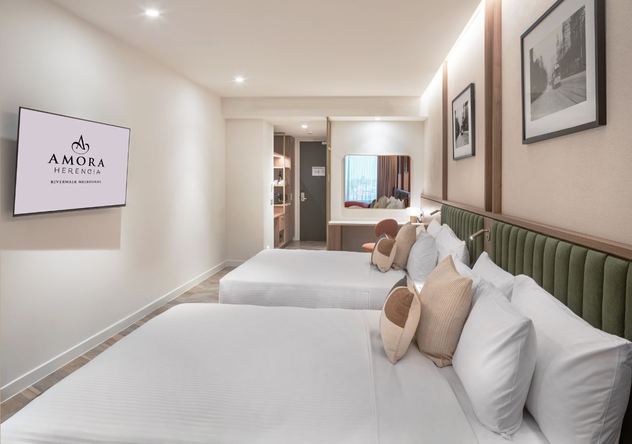 Habitación de hotel con dos camas, un espejo, cuadros en la pared y un cartel con el nombre del hotel.