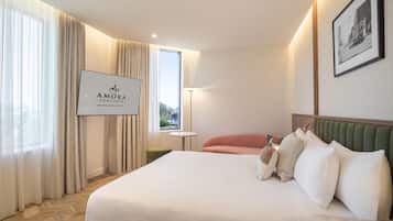 A hotel room with a bed, a nightstand, a lamp, a window with curtains, and a sign on the wall.