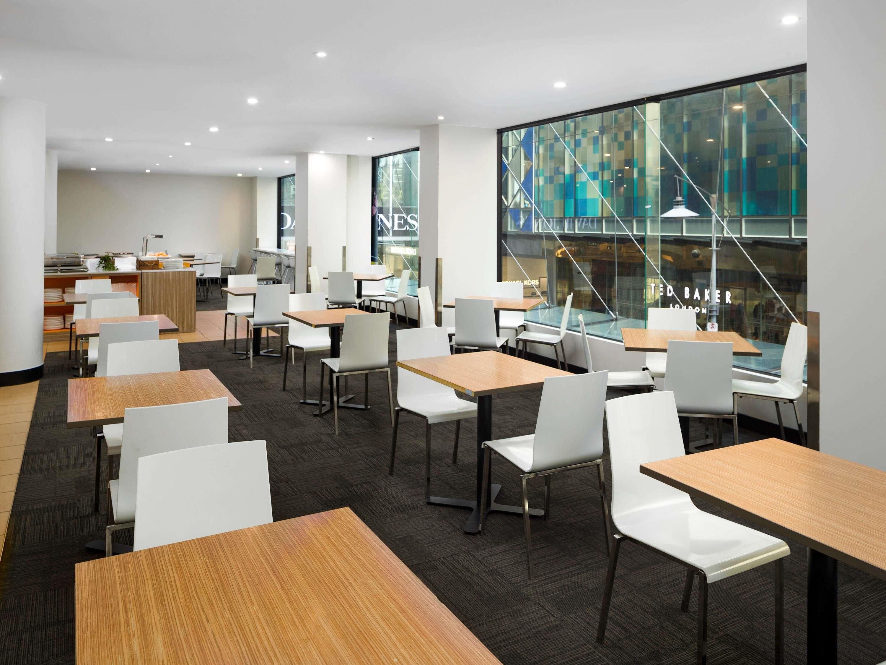 A modern dining area with multiple tables and chairs, large windows with a view of buildings, and a counter with a menu.
