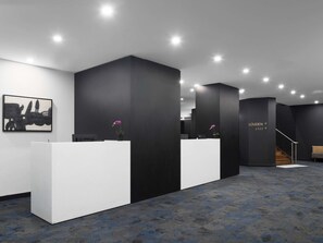 Una moderna zona de recepción con dos mostradores blancos, paredes de acento negro y una escalera que conduce a un nivel superior.