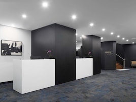 Una moderna zona de recepción con dos mostradores blancos, paredes de acento negro y una escalera que conduce a un nivel superior.