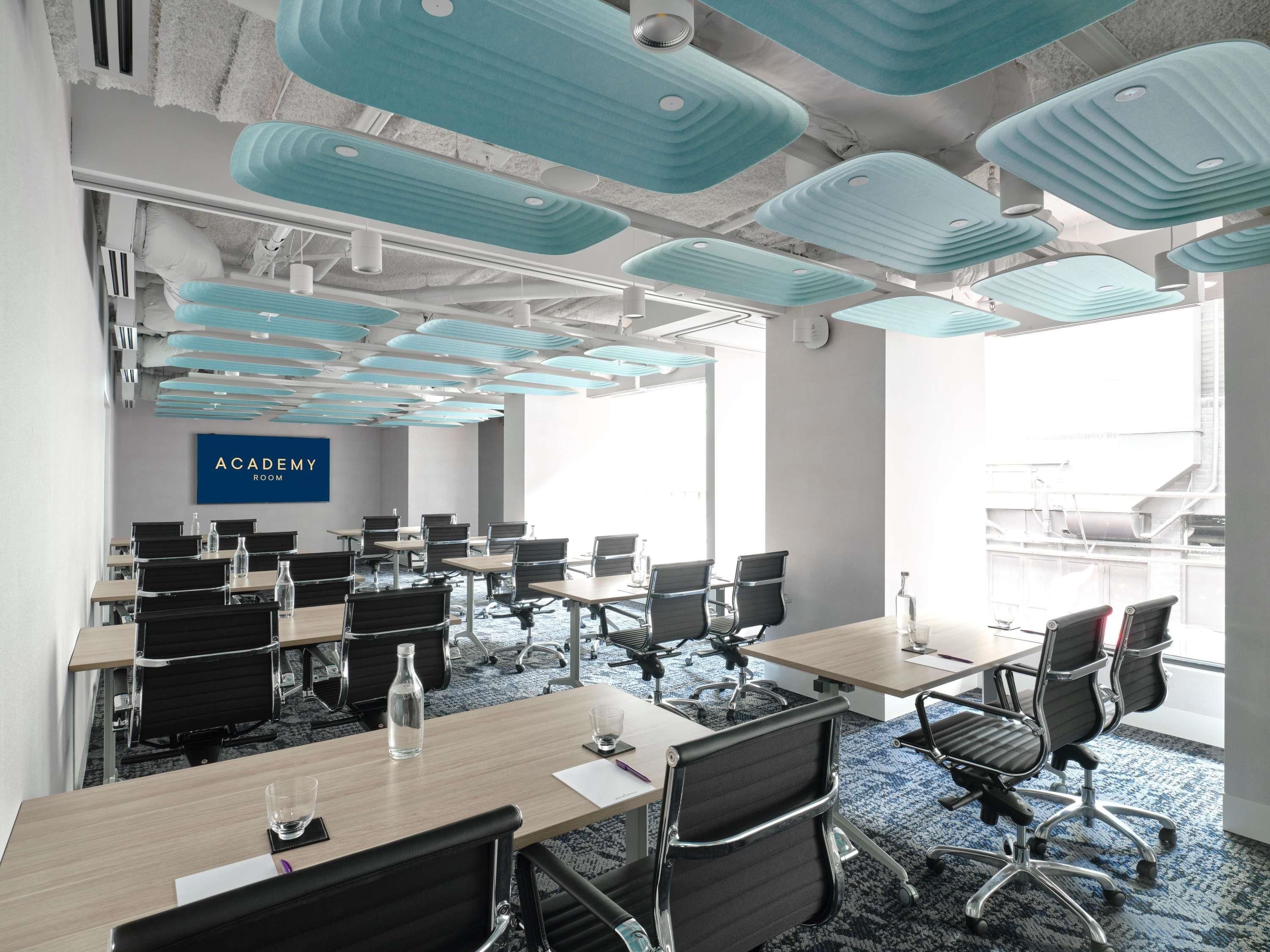 Une salle de conférence dotée d’un plafond au design moderne, de plusieurs tables et de chaises.