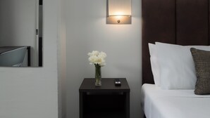 Ein Hotelzimmer mit Bett, Nachttisch mit Blumenvase, Fernbedienung und Wandleuchte.