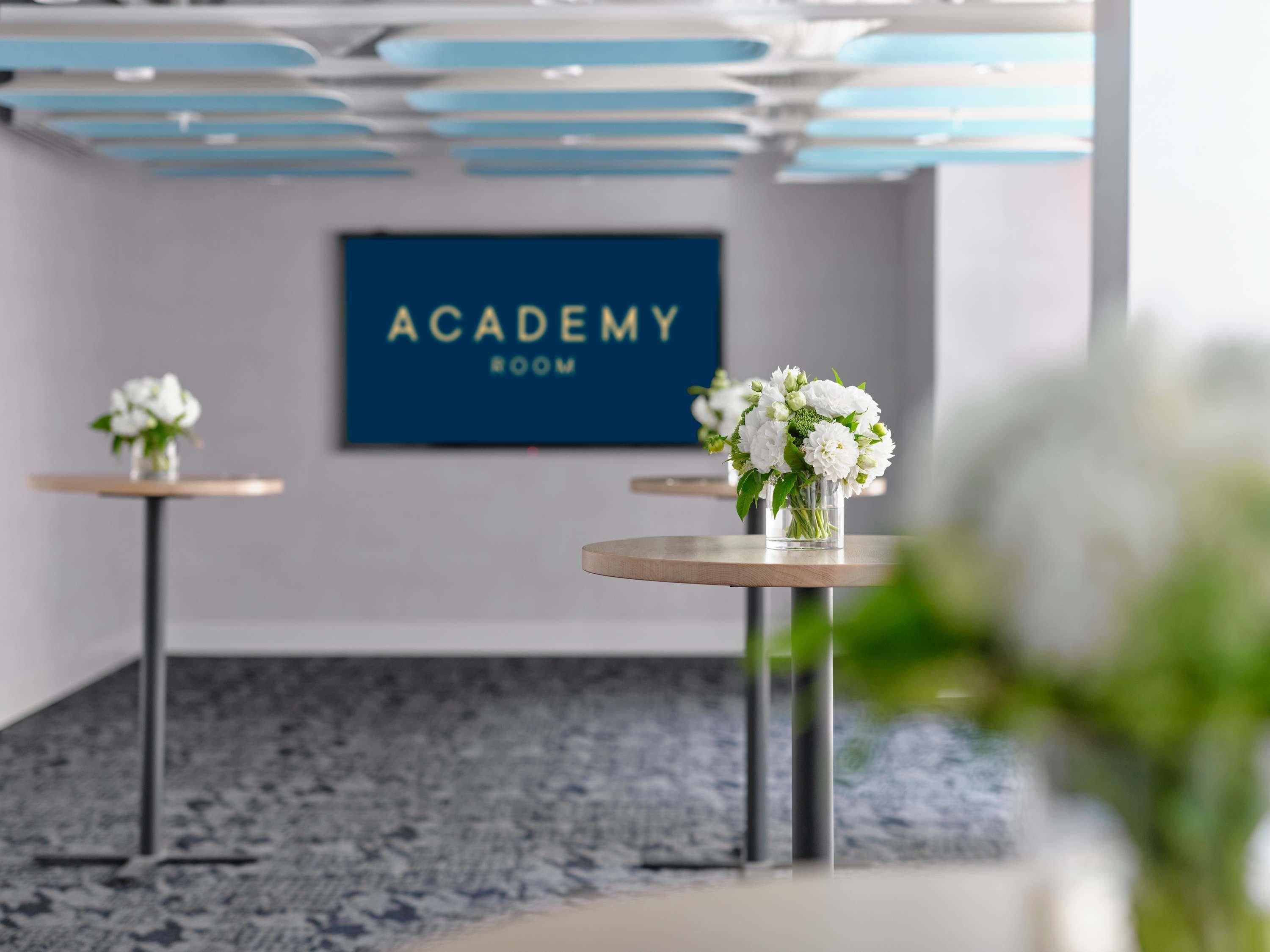 Una habitación con un letrero que dice 'ACADEMY ROOM', dos pequeñas mesas con jarrones de flores y un piso de mármol.