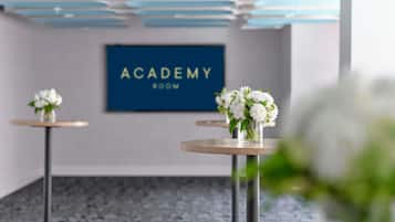 Una habitación con un letrero que dice 'ACADEMY ROOM', dos pequeñas mesas con jarrones de flores y un piso de mármol.