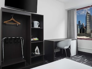 A modern hotel room with a dark wood wardrobe, a desk, a white chair, and a city view through a large window. - Mercure Melbourne City Centre (Melbourne)
