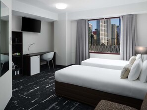 Habitación de hotel con cama, escritorio, silla, televisor y ventana con vista a la ciudad.