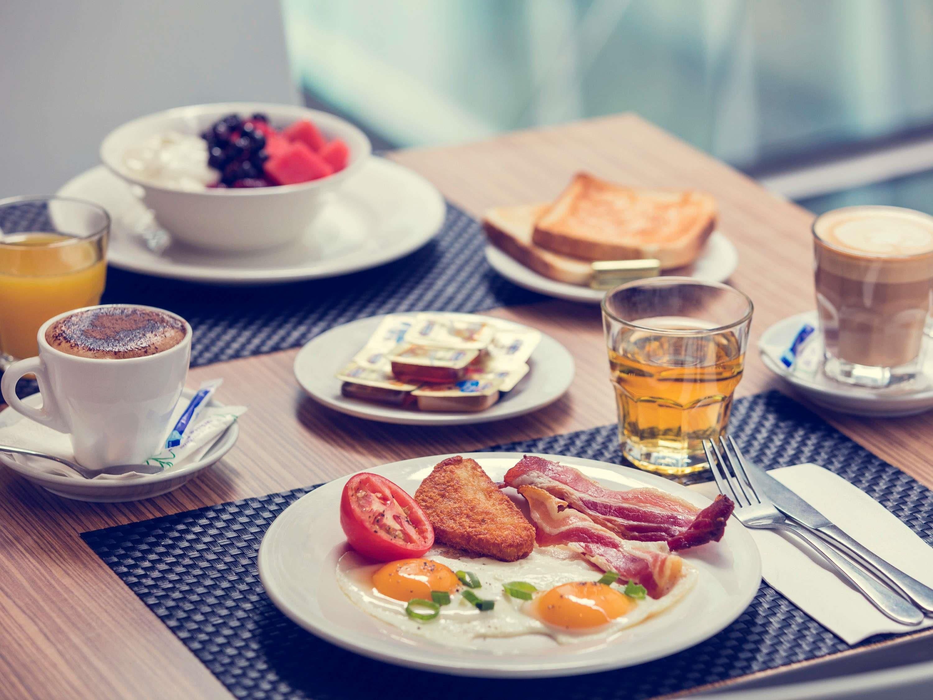 Un desayuno con huevos, tocino, tostadas, un bol de fruta, una taza de café y un vaso de jugo.