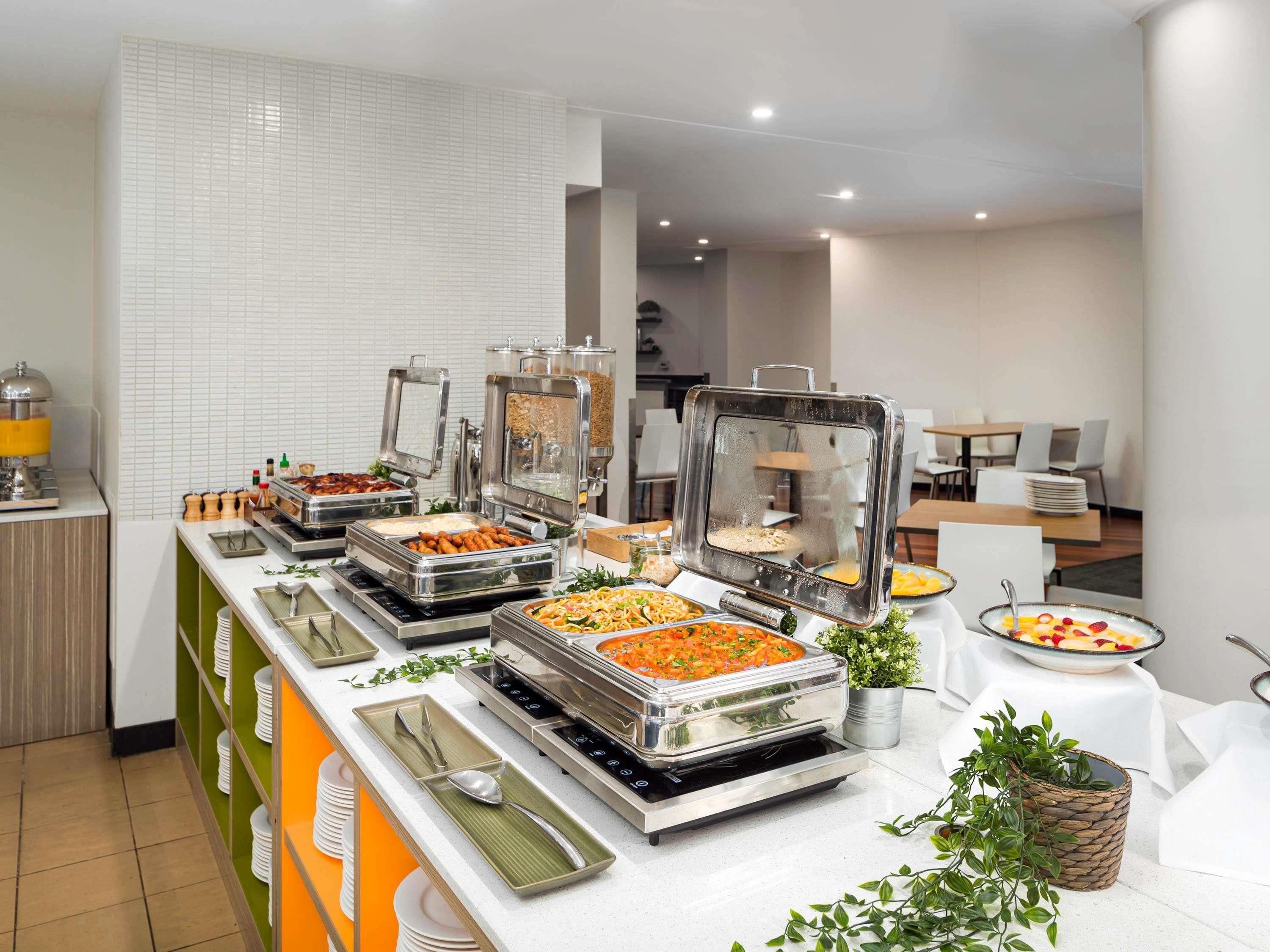 A buffet setup with various food stations, including a salad bar, a hot dish station, and a fruit bowl.