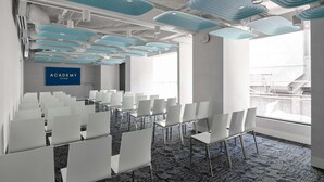 Ein Konferenzraum mit Reihen weißer Stühle, einem blauen Schild mit der Aufschrift 'ACADEMY ROOM' und einem gemusterten Teppich.