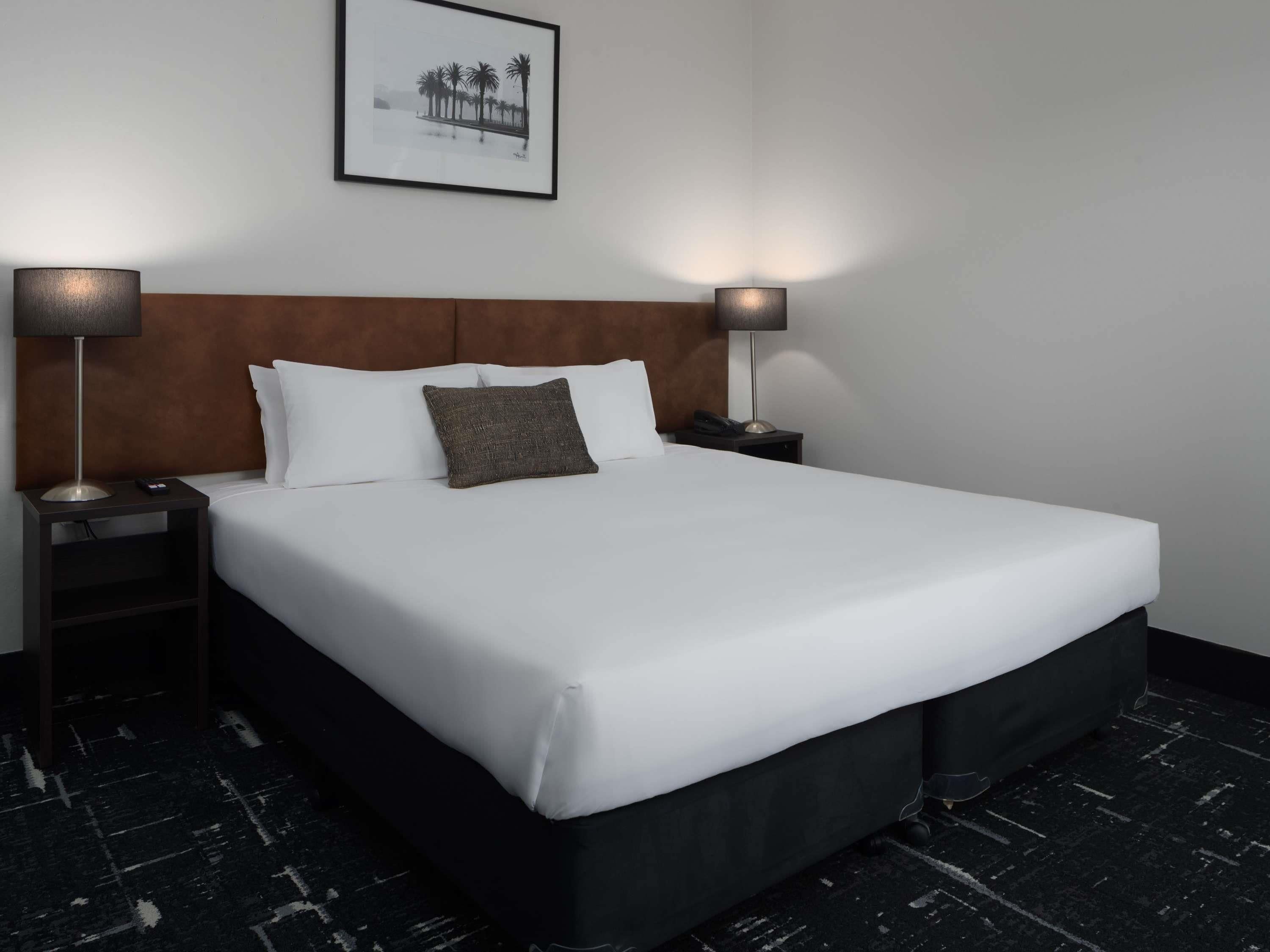 A hotel room with a large bed, two bedside tables, a headboard, and a framed picture on the wall.