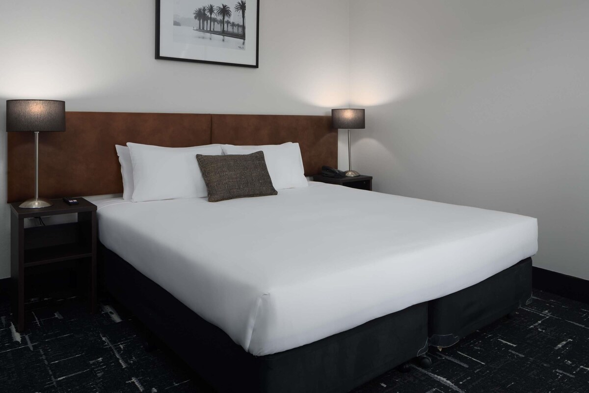A hotel room with a large bed, two bedside tables, a headboard, and a framed picture on the wall.