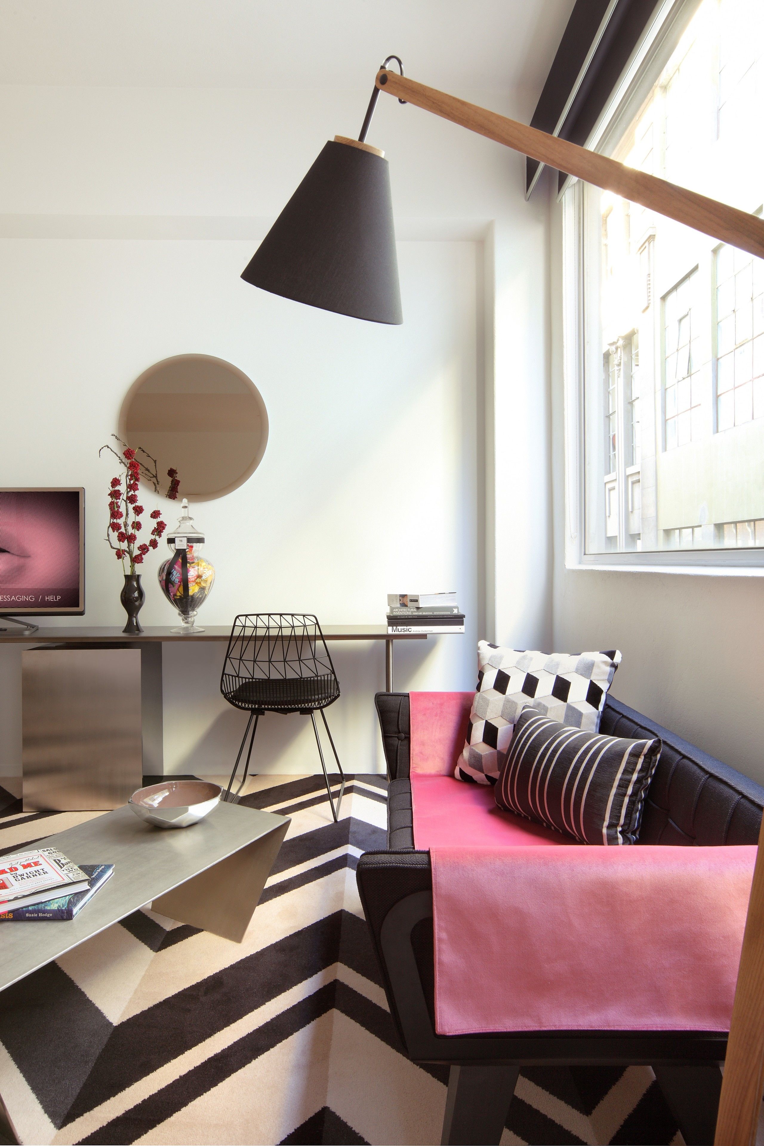 A modern living room with a sofa, a desk, a lamp, and a view of the city through a window.
