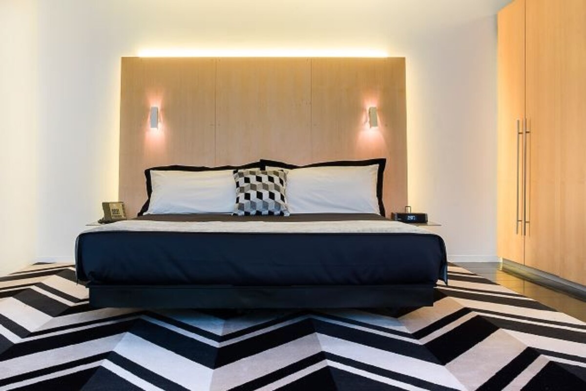Un dormitorio moderno con una cama grande, dos lámparas de noche y una alfombra con estampado geométrico.