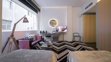 A modern hotel room with a bed, a desk, a chair, and a TV.