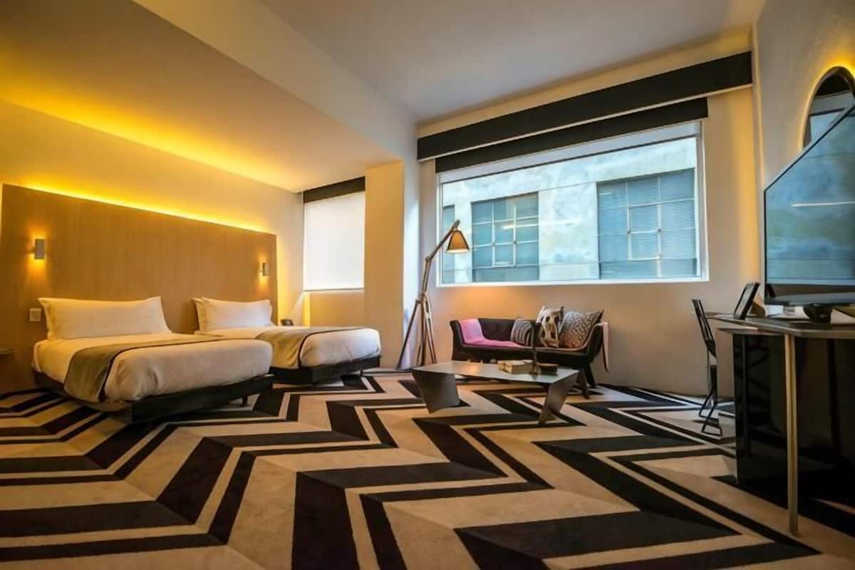 A hotel room with a bed, a sofa, a desk, and a large window.