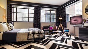 A modern hotel room with a large bed, a desk, a chair, a TV, and a large window with curtains. - Adelphi Hotel (Melbourne)