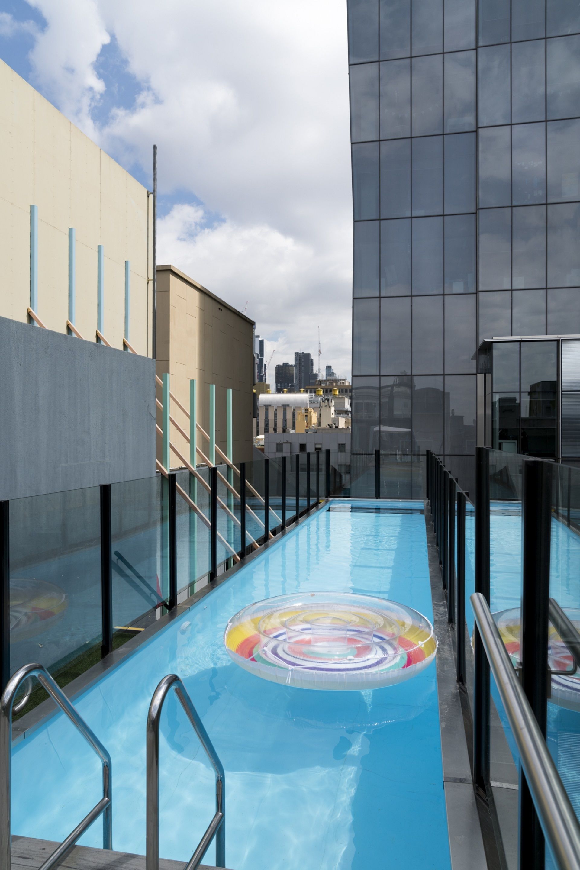 Une piscine sur le toit, dotée d’une barrière en verre, de rampes métalliques et d’un motif circulaire coloré sur le sol.