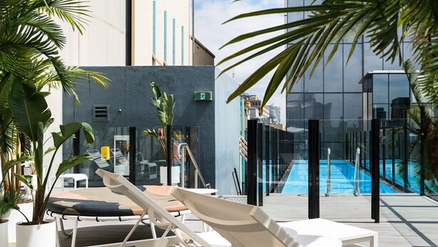 A rooftop pool area with lounge chairs, potted plants, and a glass building in the background. - Adelphi Hotel (Melbourne)