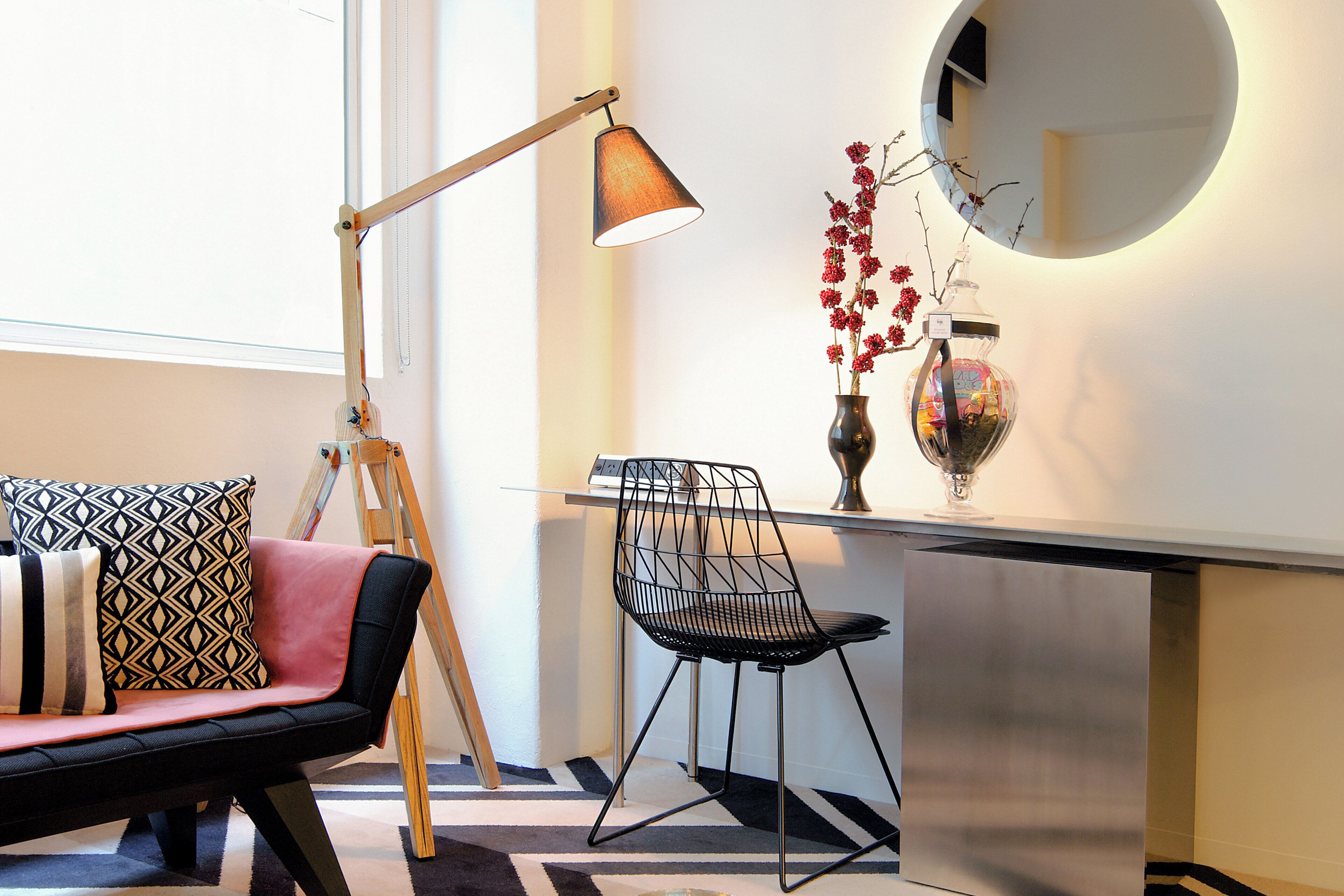 Un salon moderne avec un canapé, un fauteuil noir, une lampe sur pied et un vase rempli de fleurs rouges.