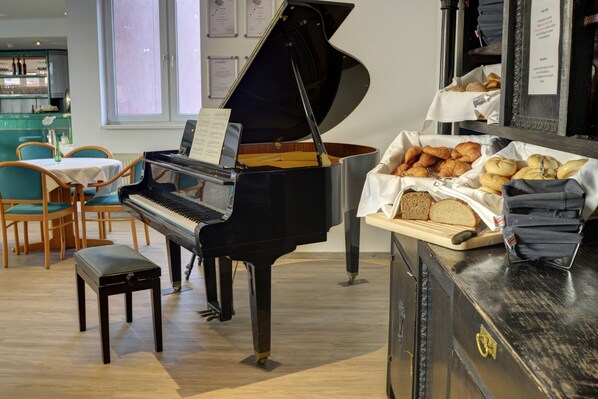 A piano in a room with a table of pastries and a piano bench.