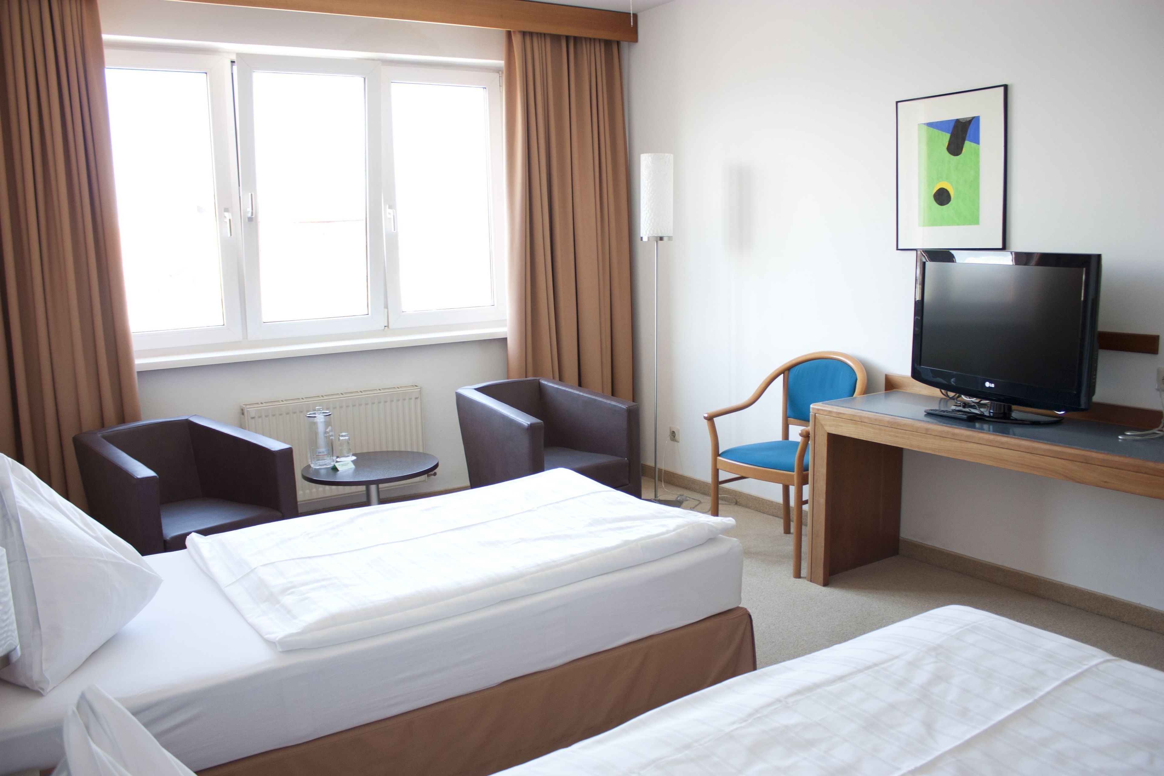 Une chambre d’hôtel avec deux lits, un bureau avec une télévision, une chaise et une fenêtre avec des rideaux.