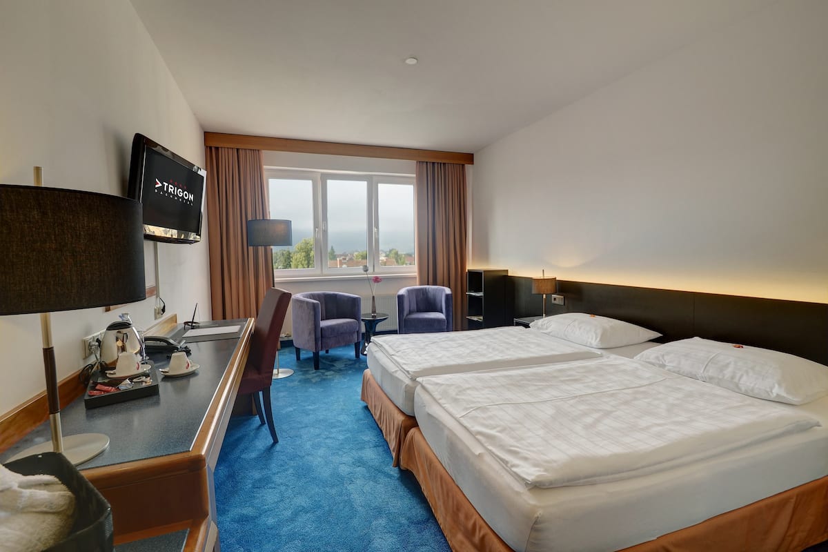 Habitación de hotel con dos camas, un escritorio con cafetera, televisor y vista a la ciudad.
