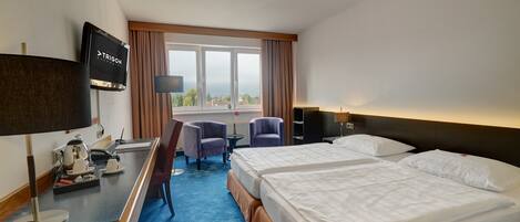 A hotel room with two beds, a desk with a coffee maker, a TV, and a view of the city.