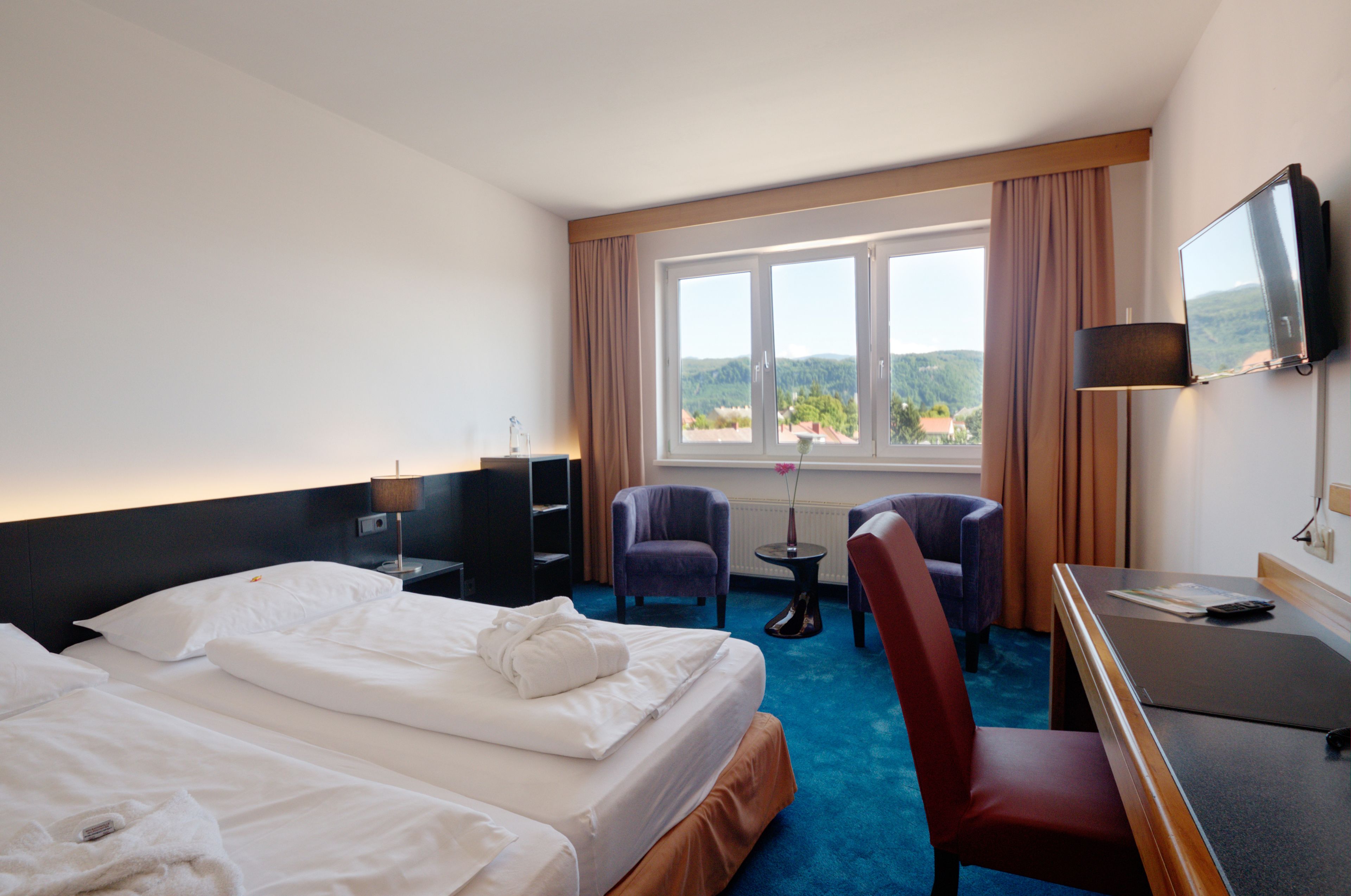 Hotellihuone, jossa on kaksi sänkyä, työpöytä, televisio ja näkymä ulos.