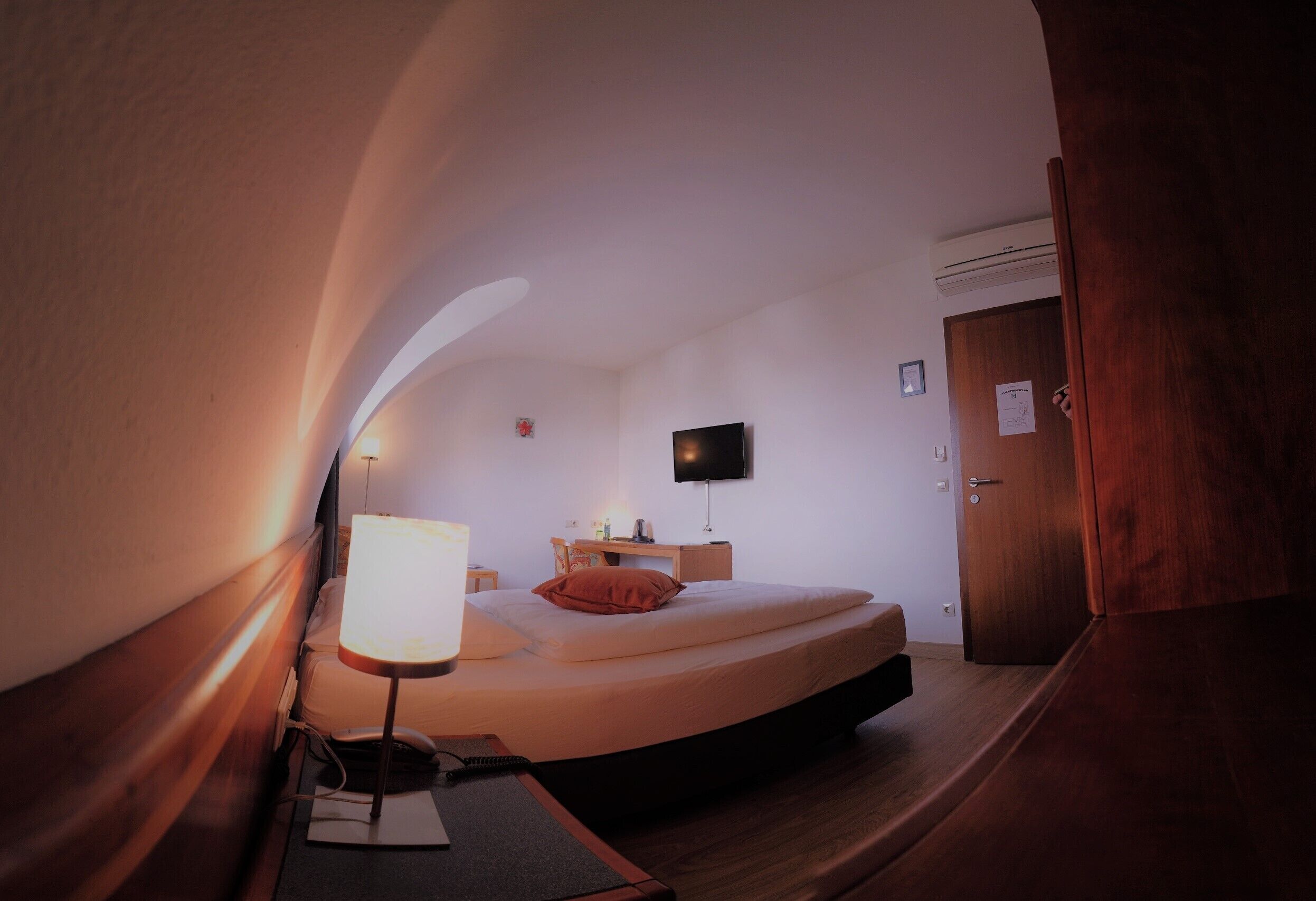Ein Schlafzimmer mit einem Bett, einem Nachttisch, einer Lampe und einem Fernseher an der Wand.