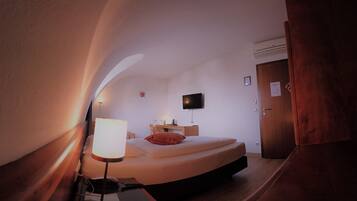 Ein Schlafzimmer mit einem Bett, einem Nachttisch, einer Lampe und einem Fernseher an der Wand.