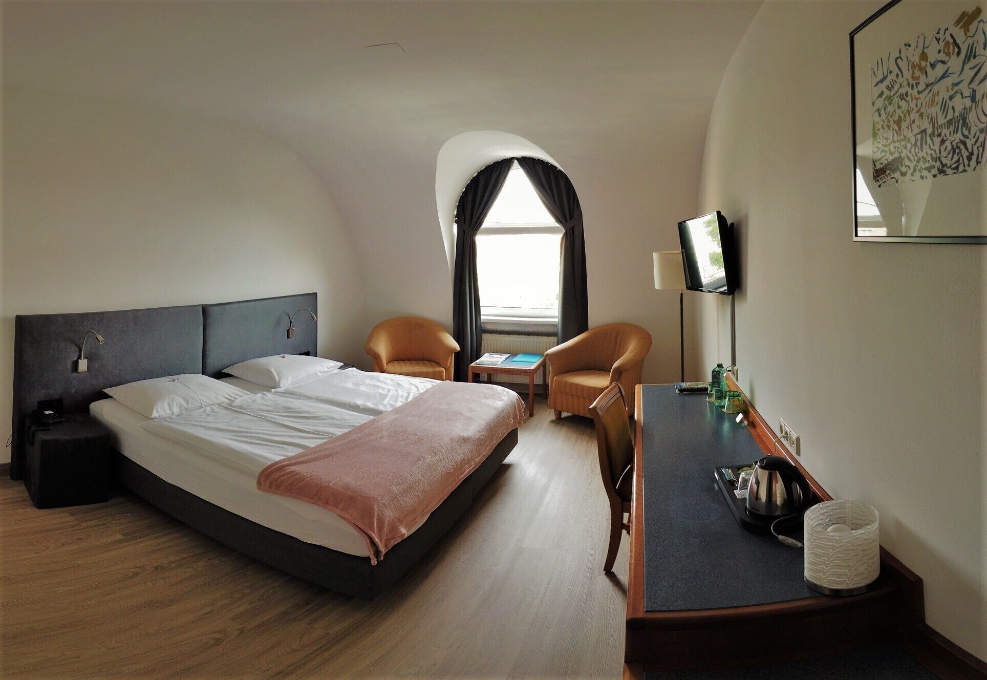 Una habitación de hotel con cama, dos sillones, una mesita, televisor y ventana con cortinas.