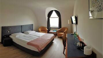 Una habitación de hotel con cama, dos sillones, una mesita, televisor y ventana con cortinas.