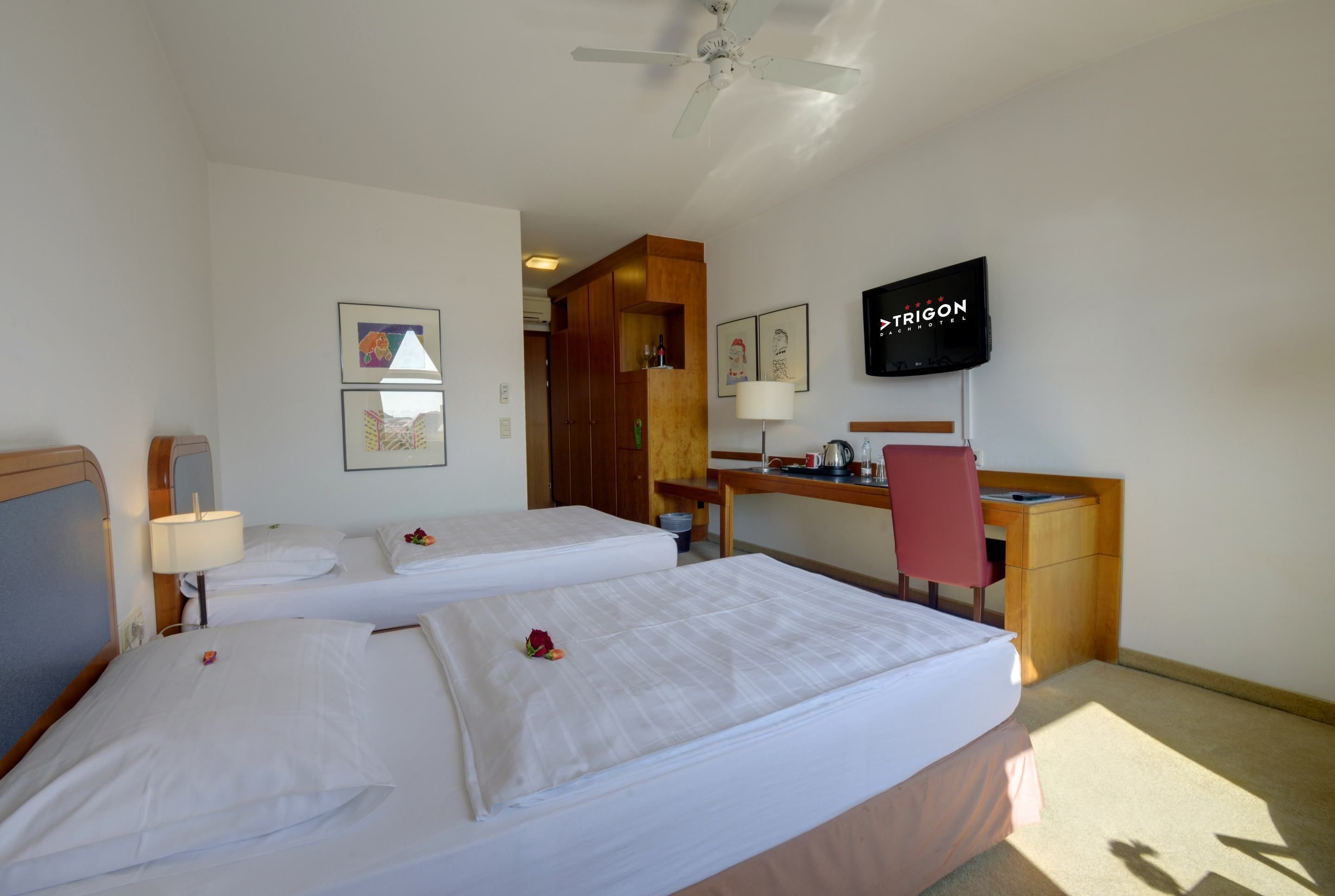 Habitación de hotel con dos camas, un escritorio, una silla, un televisor y un ventilador de techo.