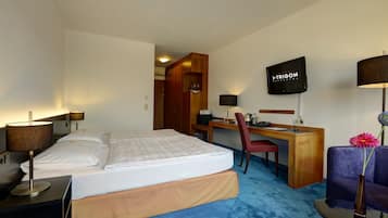 Une chambre d’hôtel avec un lit, un bureau, une chaise, une télévision et un vase avec une fleur.