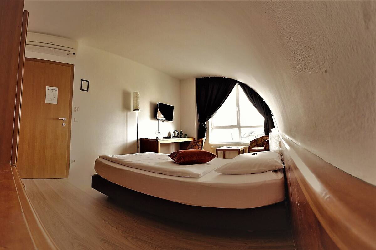 Habitación pequeña y con techo inclinado, con cama, escritorio, silla y ventana.