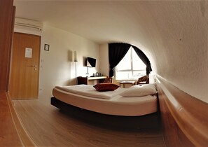 A compact, sloped room with a bed, a desk, a chair, and a window.