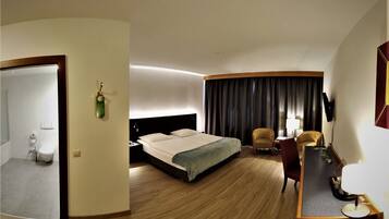 A hotel room with a bed, a desk, a chair, a mirror, and a bathroom visible through an open door.