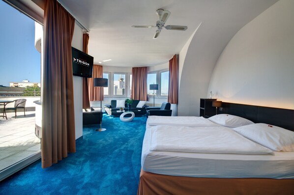 A modern hotel room with a large bed, a sofa, a TV, and a balcony with a view of the city.