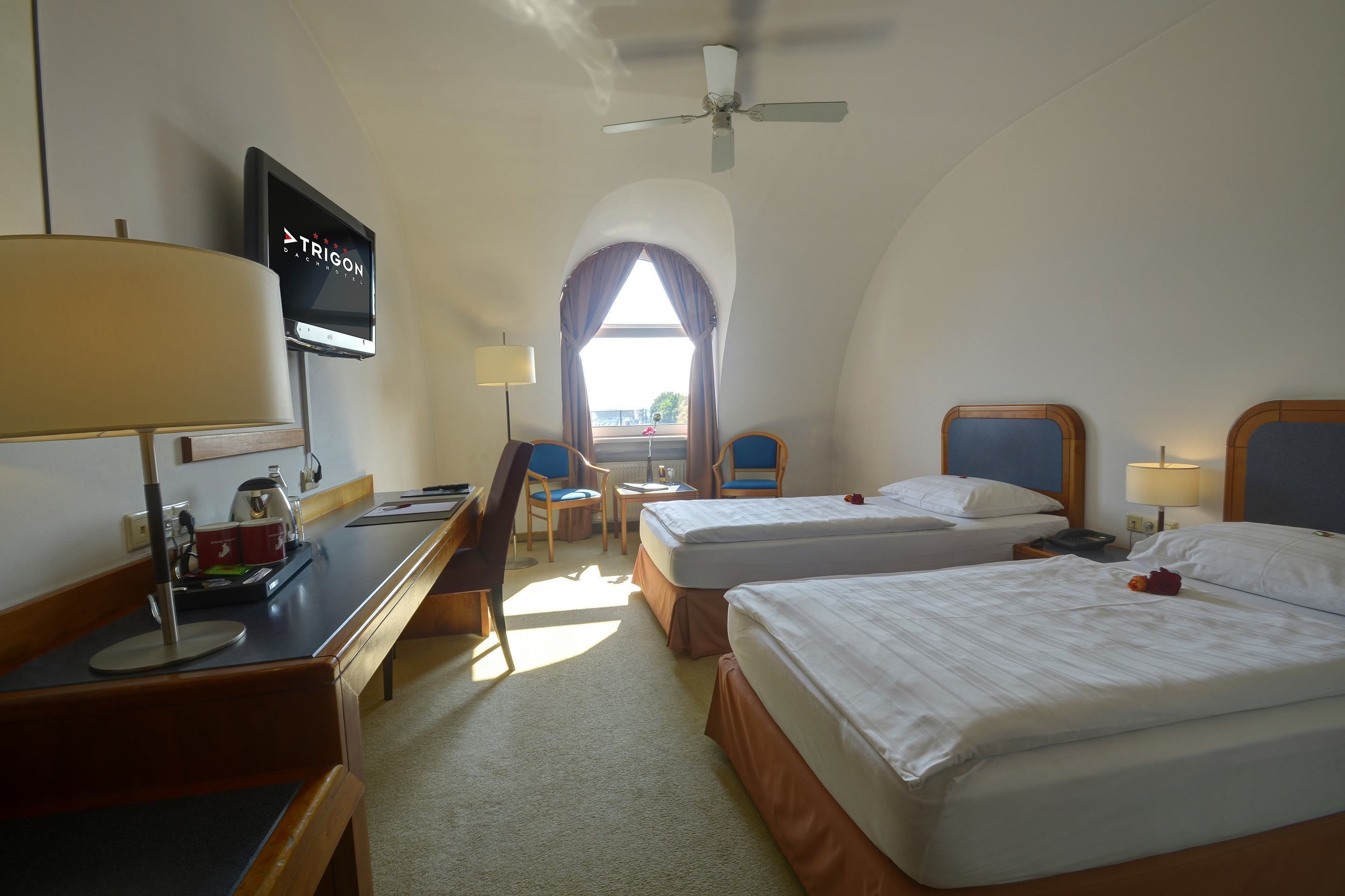 A hotel room with two beds, a desk with a TV, a chair, and a window with curtains.