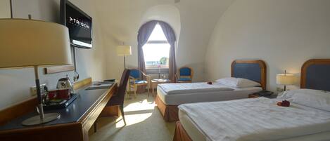 A hotel room with two beds, a desk with a TV, a chair, and a window with curtains.