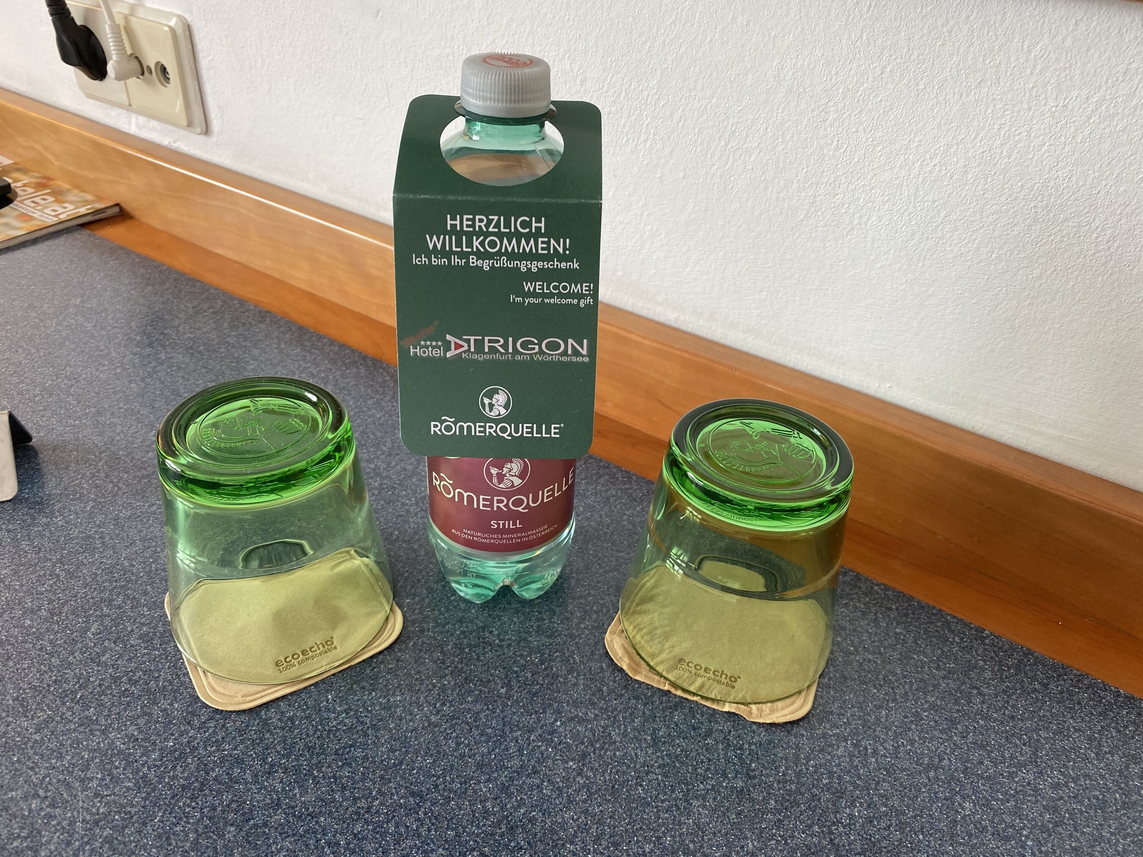 Un obsequio de bienvenida del hotel con una botella de agua mineral Römersquelle y dos recipientes de vidrio con tapas ecológicas.