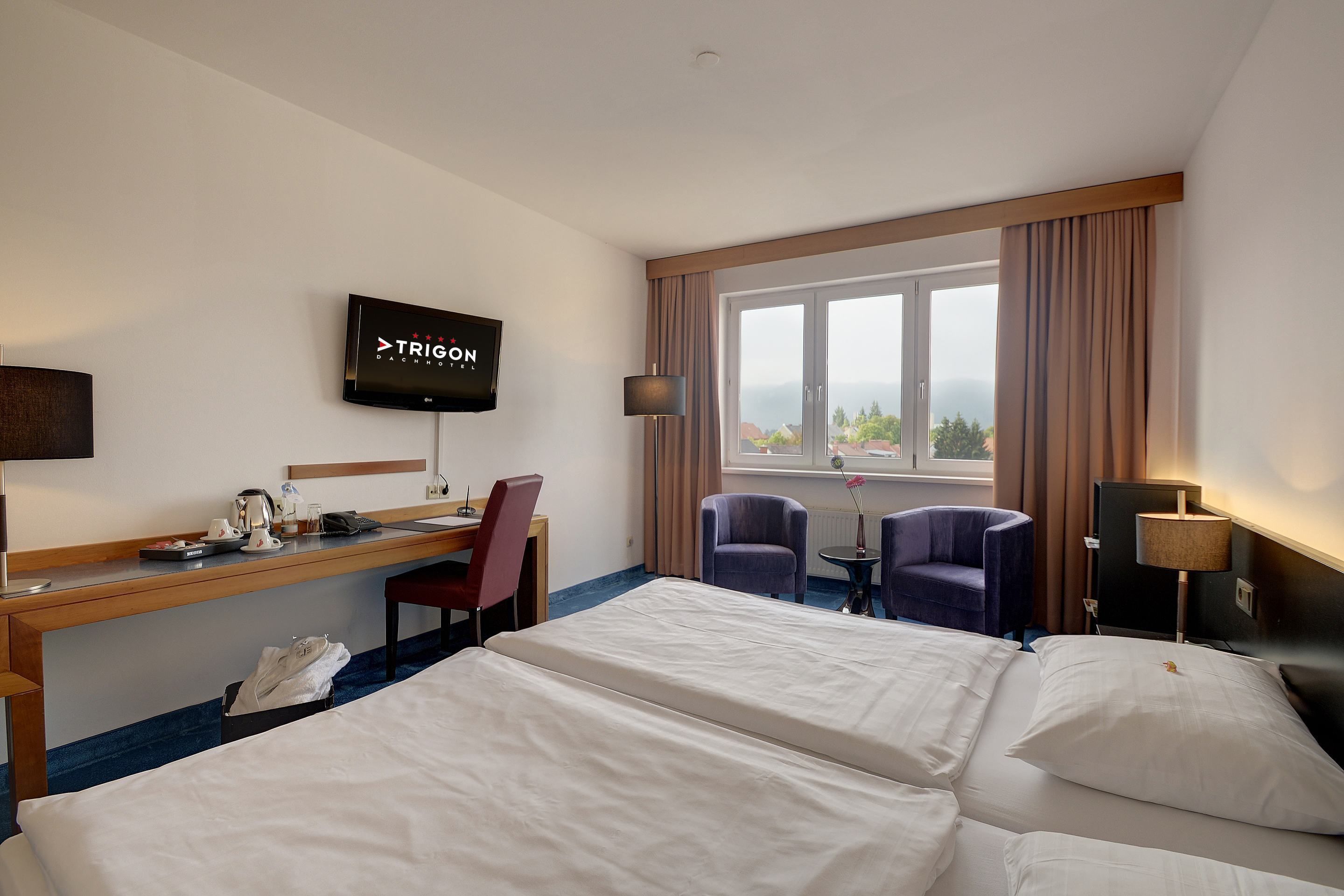 A hotel room with two beds, a desk with a chair, a TV, and a window with curtains.